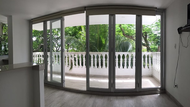 Une pièce dotée d’une porte en verre incurvée qui donne sur un balcon agrémenté d’une balustrade blanche et de plantes.