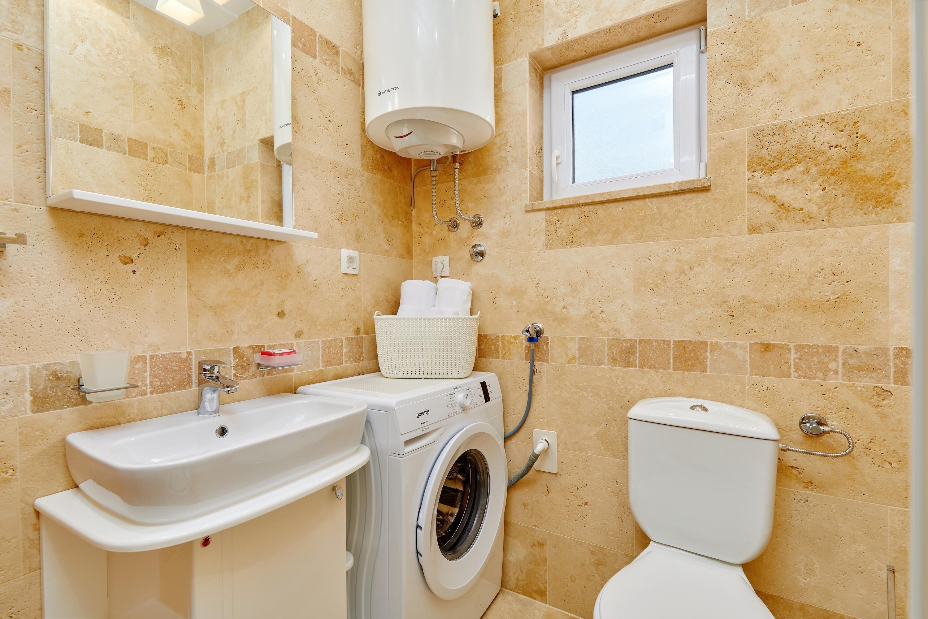 A bathroom with a washing machine, a toilet, a sink, and a window.