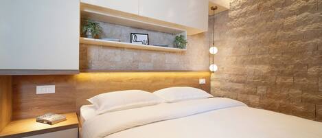 A modern bedroom with a stone accent wall, a bedside table with a book, and a shelf with decorative items.