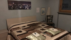 A bedroom with a bed, a chair, a window, and a cityscape picture on the wall. - B&B Cascina Garaita (Genola)