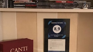 A shelf with books, a framed certificate, a microwave, and a Canti wine box. - B&B Cascina Garaita (Genola)