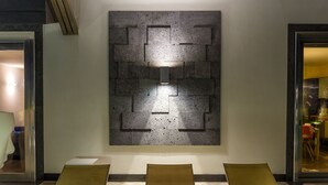 Un hall d’entrée doté d’un décor mural moderne, de trois fauteuils confortables et d’une porte vitrée donnant accès à un autre espace.