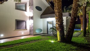 Un bâtiment moderne doté d’une entrée bien éclairée, d’un chemin pavé et d’un espace verdoyant agrémenté de palmiers.