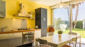 Une cuisine moderne dotée d’appareils électroménagers en acier inoxydable, un coin repas avec une table et des chaises, et une grande fenêtre offrant une vue sur l’extérieur.