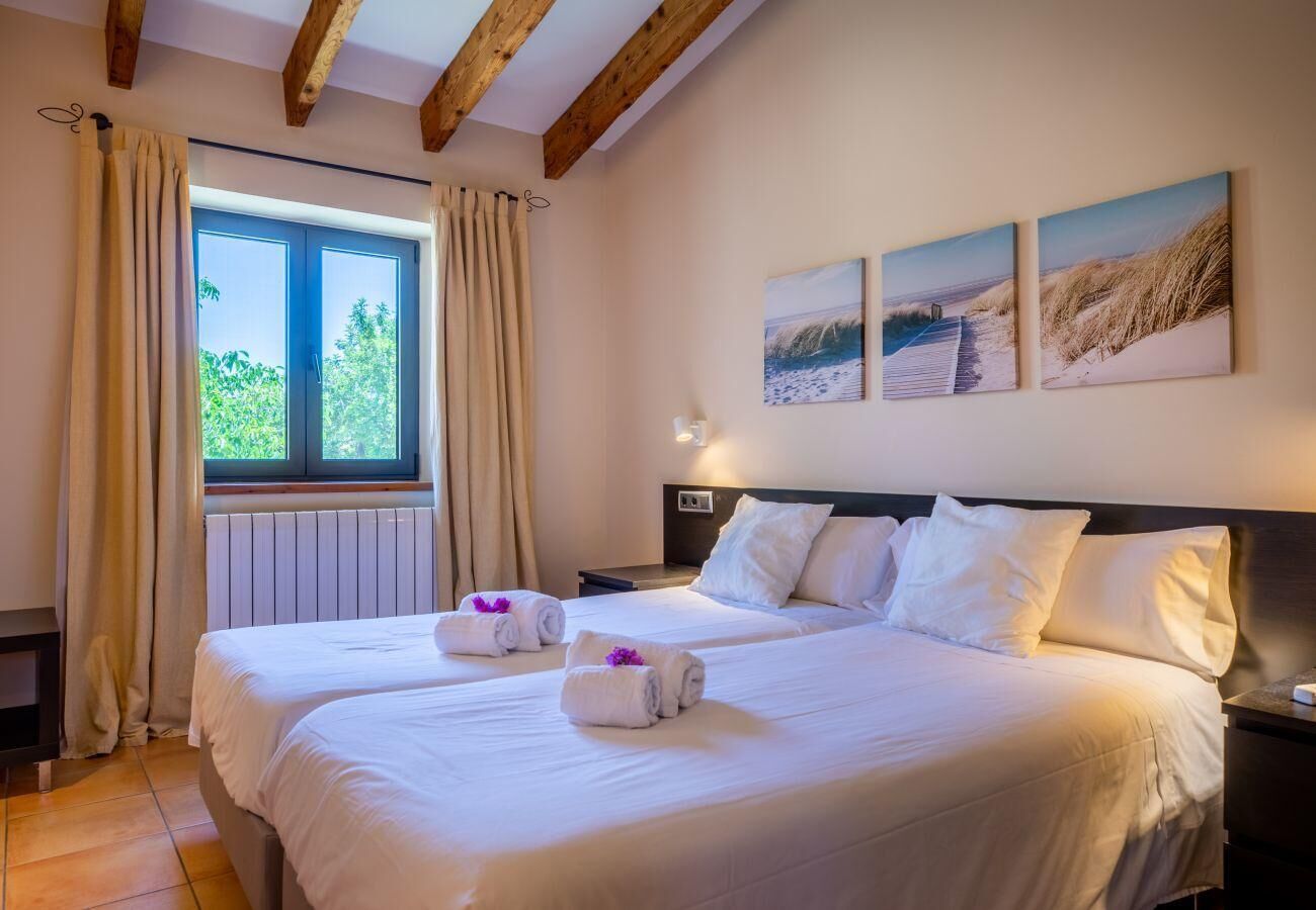 A hotel room with two beds, a window with curtains, a radiator, and wall-mounted artwork.