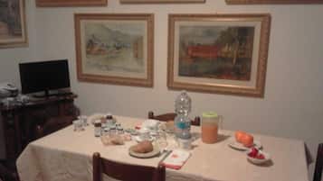 A dining table with various items, including a plate with food, a glass, and a bottle. There are framed paintings on the wall above the table.