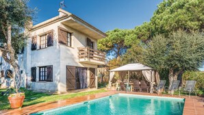 Ein zweistöckiges Haus mit Swimmingpool, Sitzgelegenheiten im Freien und einer Pergola.