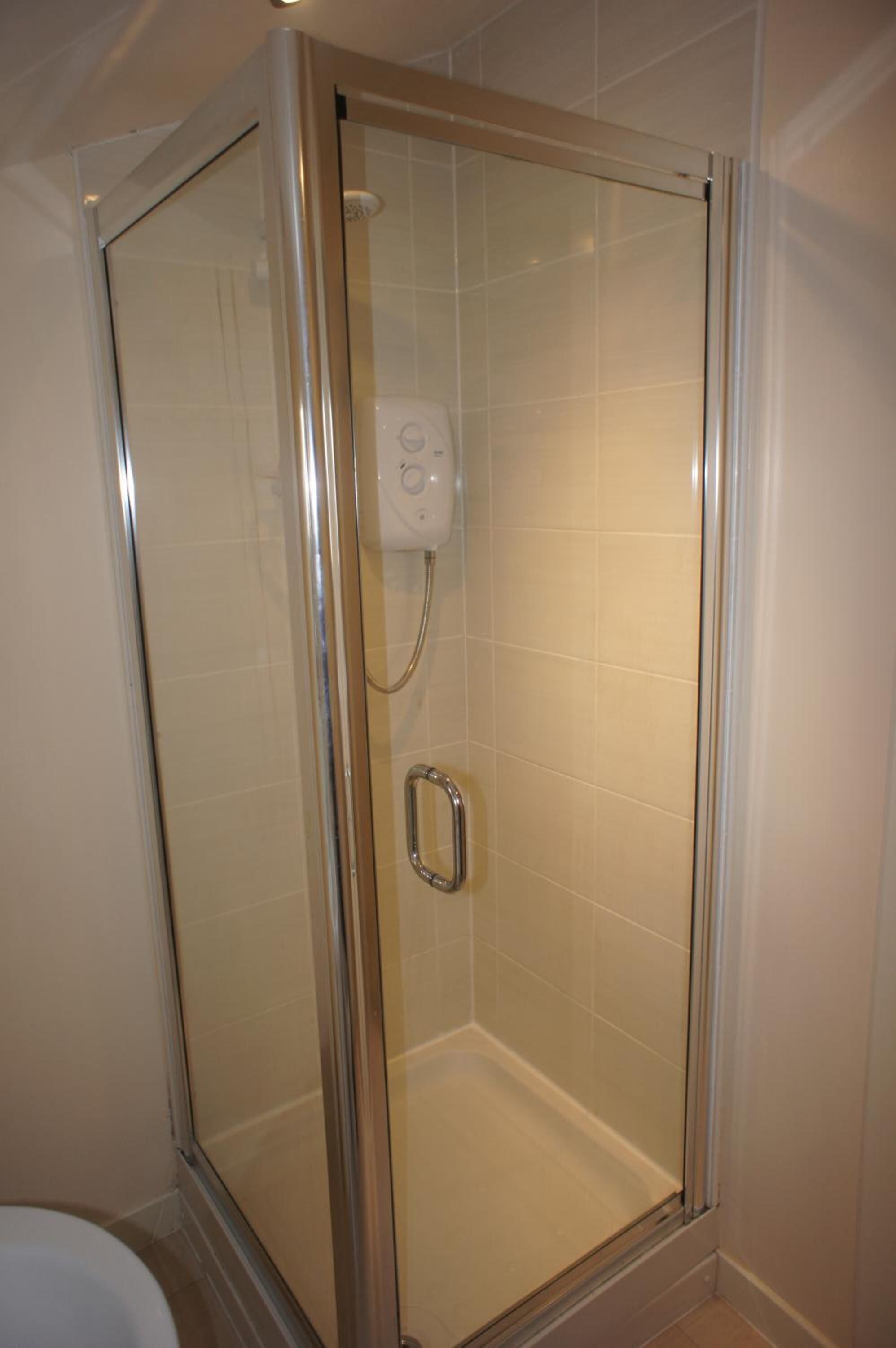 Une douche fermée par des parois en verre, dotée d’un panneau de commande et d’une barre d’appui.