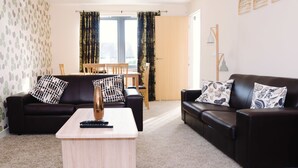 A living room with two black sofas, a wooden coffee table, and a dining area with a wooden table and chairs. - Elforma - Tudsbery House (Edinburgh)