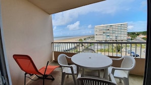 A balcony with a table and chairs, overlooking a beach and a hotel building. - 2-room apartment, sleeps 5 with balcony - Saint-Jean-de-Monts (Saint-Jean-de-Monts)