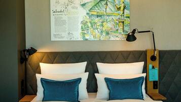 A hotel room with a bed, two pillows, a nightstand, a lamp, and a wall-mounted artwork.