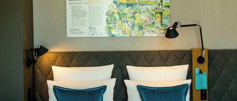 A hotel room with a bed, two pillows, a nightstand, a lamp, and a wall-mounted artwork.