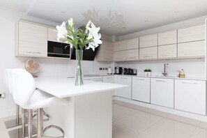 Une cuisine moderne avec des meubles blancs, un plan de travail blanc et un vase contenant des fleurs blanches.