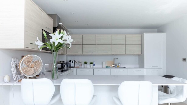 A modern kitchen with white cabinets, a white island with bar stools, and a fan. - Luxurious Central Edinburgh Apartment - Sleeps 6 (Edinburgh)