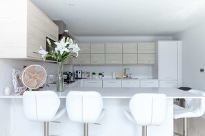 A modern kitchen with white cabinets, a white island with bar stools, and a fan. - Luxurious Central Edinburgh Apartment - Sleeps 6 (Edinburgh)