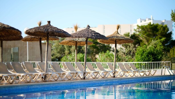 A swimming pool with lounge chairs and thatched umbrellas. -    AluaSun Cala Antena – All Inclusive (Manacor)