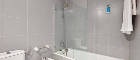 Een moderne badkamer met een douchecabine van glas, een wit bad en een wit toilet.