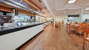 A modern cafeteria with a long counter, multiple seating areas, and a kitchen in the background.
