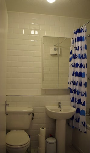 A small bathroom with a toilet, sink, and a shower curtain with a whale pattern.