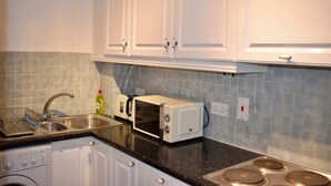 A kitchen with white cabinets, a microwave, a toaster, a sink, and a dish rack.