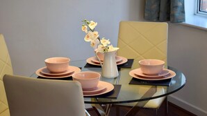 A dining area with a round glass table, pink plates, and bowls, and a vase with flowers.