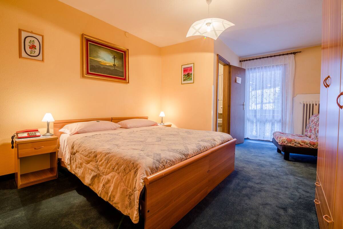 A bedroom with a wooden bed, bedside tables with lamps, a radiator, and a window with curtains.