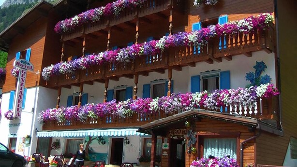 A hotel with multiple balconies adorned with flowers, a sign indicating it is a hotel, and a visible entrance with a sign. - Albergo Genzianella (Rocca Pietore)