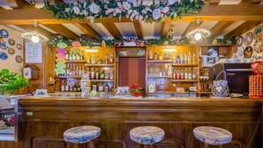 A bar area with wooden bar stools, shelves of liquor bottles, and a coffee machine. - Albergo Genzianella (Rocca Pietore)