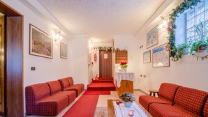A living room with red patterned sofas, a wooden coffee table, and a red carpet. - Albergo Genzianella (Rocca Pietore)
