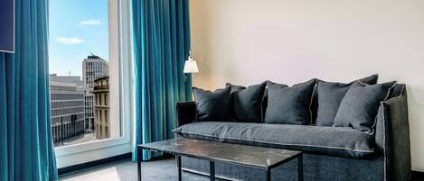 A modern room with a sofa, a small table, and a view of the cityscape through a large window.