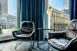 A room with two leather chairs, a small table, and a view of city buildings through large windows. - Motel One Frankfurt-Römer (Frankfurt)