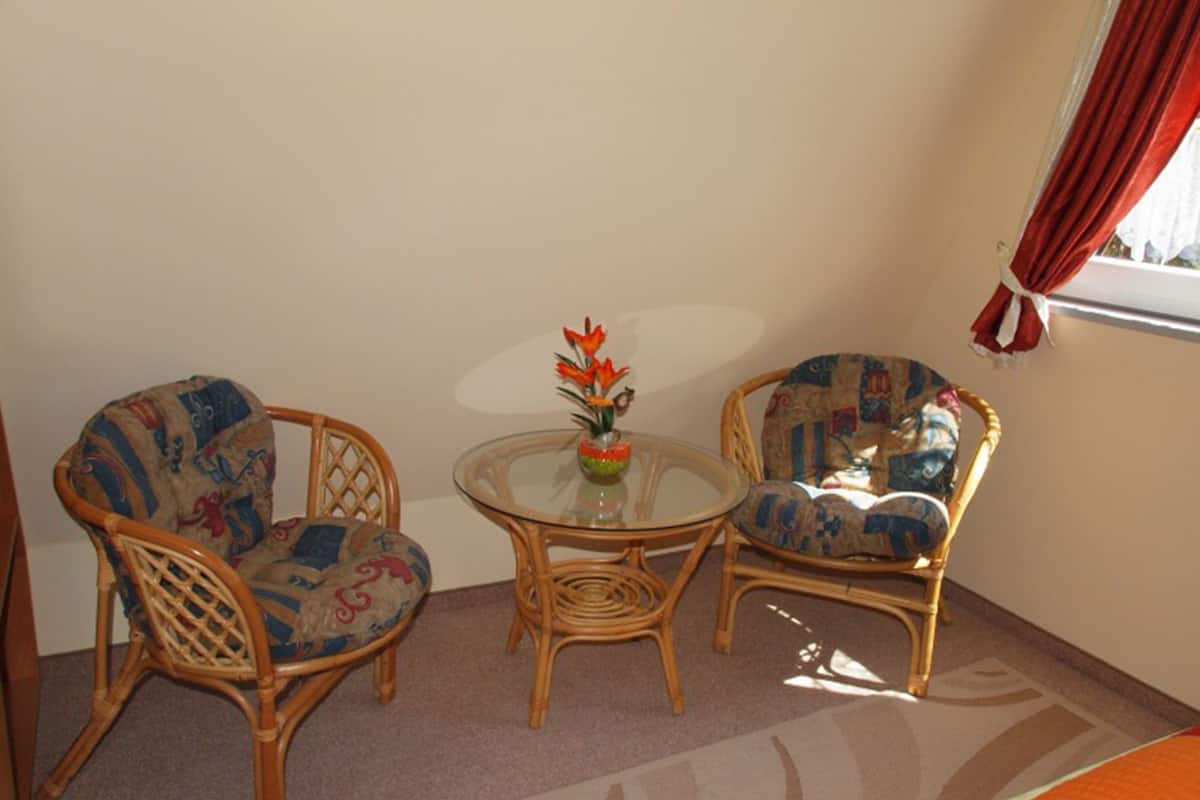 Une pièce avec deux fauteuils en osier et une table en verre, un vase rempli de fleurs et une fenêtre ornée de rideaux rouges.