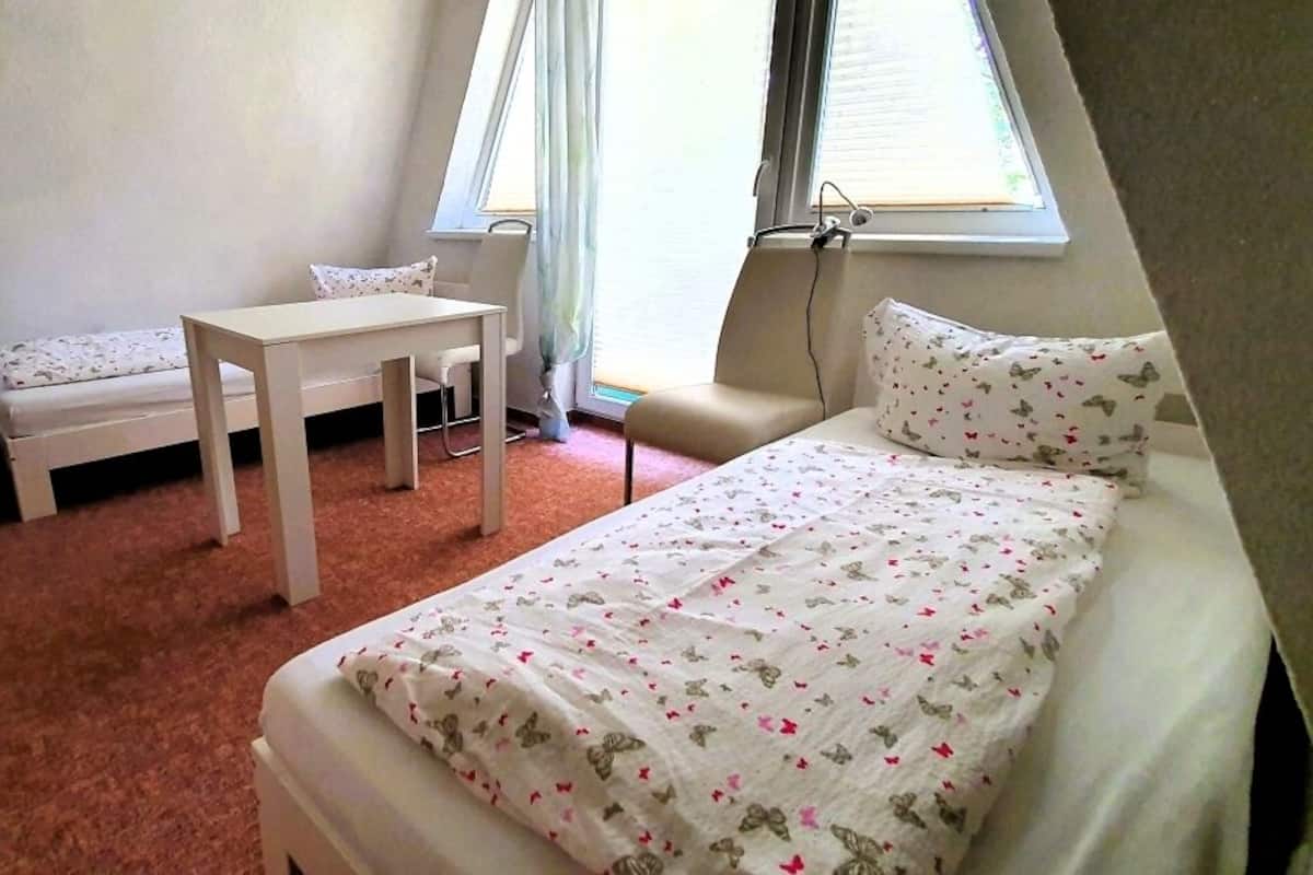 Une petite pièce, bien rangée, avec un lit, un bureau, une chaise et une petite table.