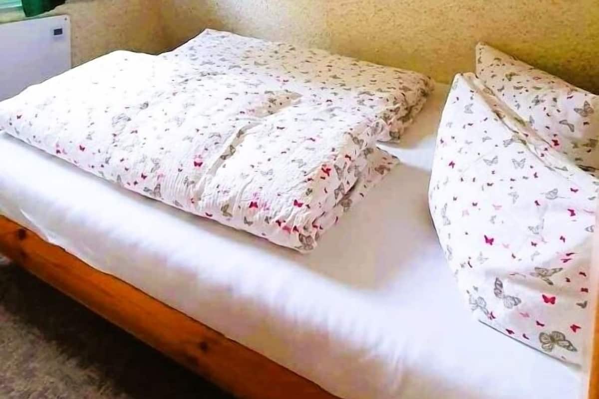 Un lit simple avec une literie à motifs floraux, une tête de lit en bois et un luminaire fixé au plafond.