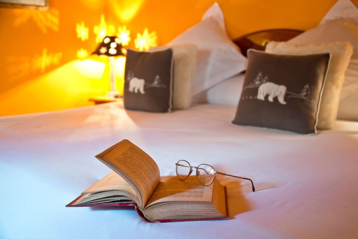 Ein Bett mit Buch, Brille, Kissen mit Tiermotiven, einer Lampe.