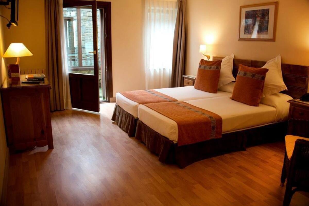 Ein Hotelzimmer mit einem Doppelbett, zwei Nachttischen mit Lampen, Holzboden und einem fenster mit Vorhängen.