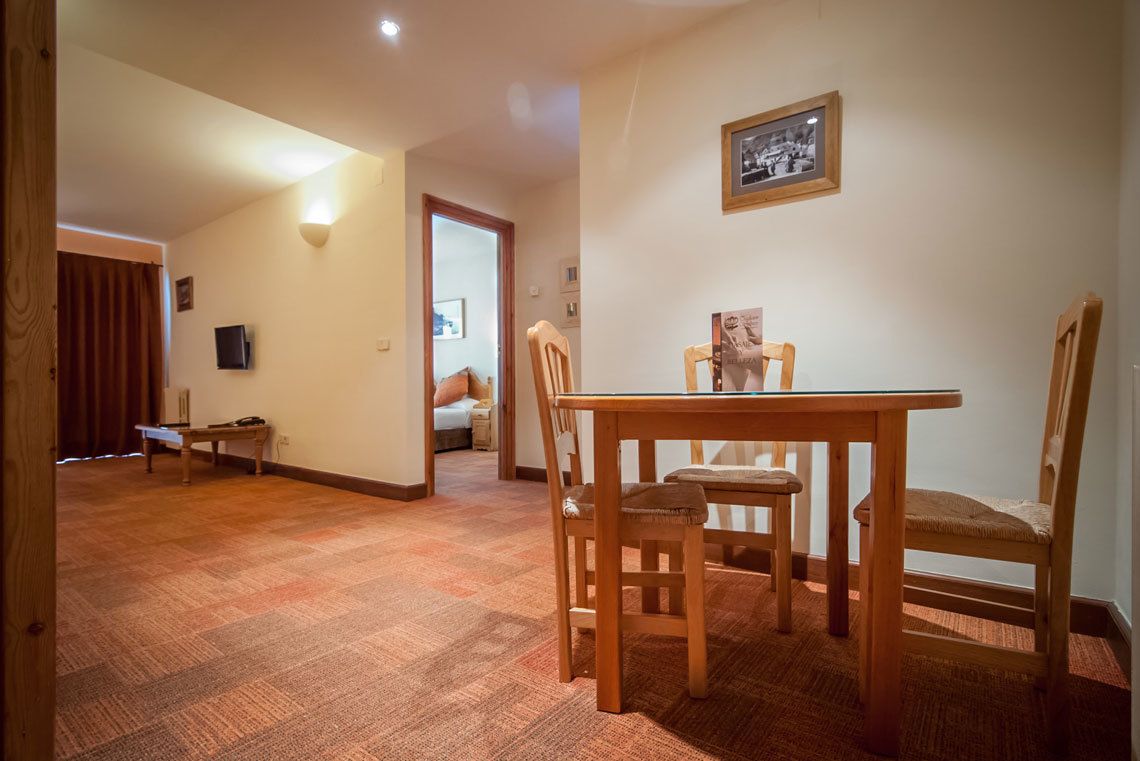 A dining area with a wooden table and chairs, a framed picture on the wall, and a carpeted floor.