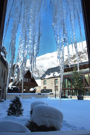 Paisagem nevada com icicles pendendo de uma janela, uma montanha ao fundo e um prédio com fachada de madeira.