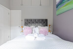 A neatly made bed with a tufted headboard, white bedding, and pink decorative pillows.