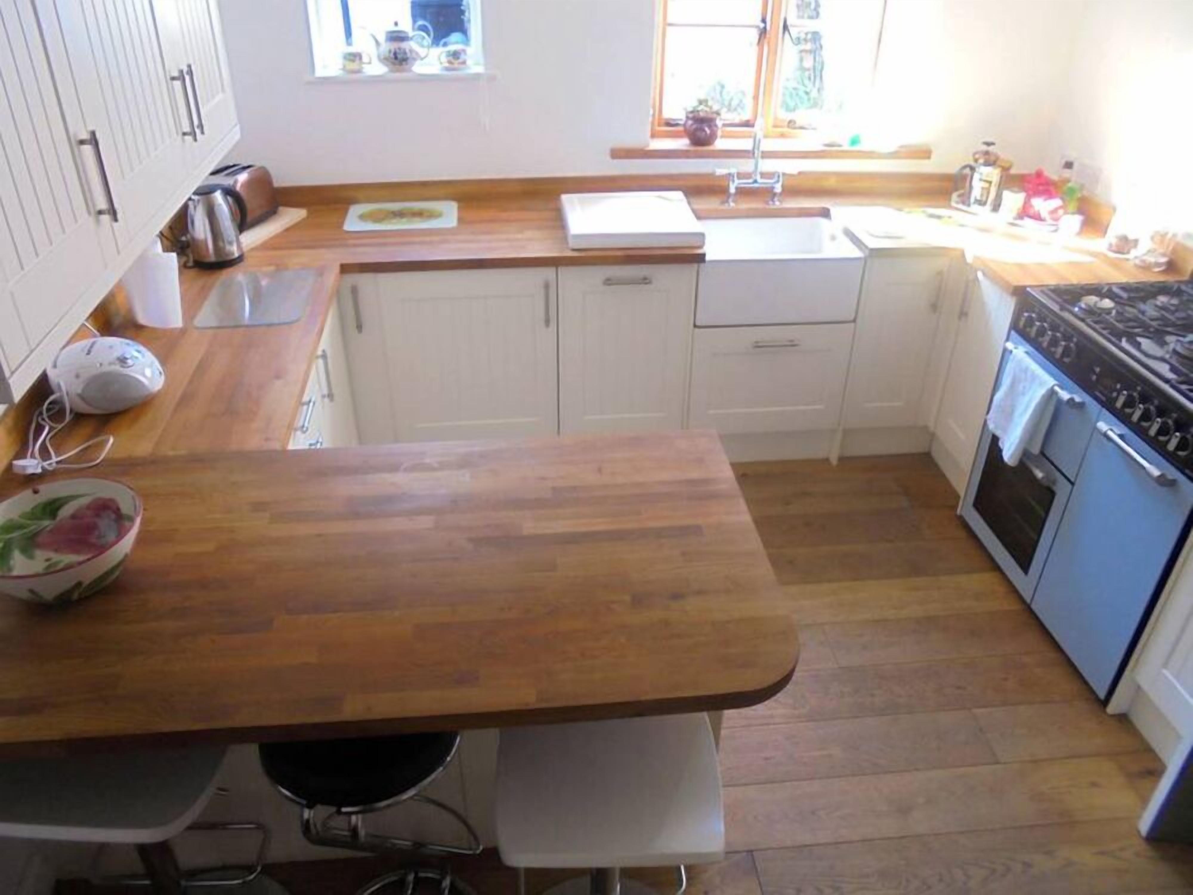 Une cuisine de taille réduite, dotée de plans de travail en bois, d’un évier, d’une cuisinière et d’armoires blanches.