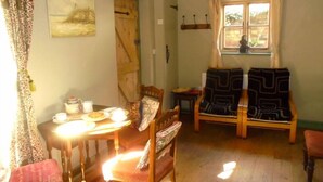 Una habitació acollidora amb una taula de fusta preparada per al te, dues cadires, una finestra amb cortines i un quadre al mur.