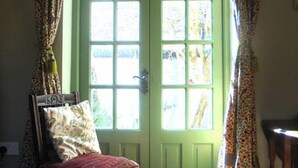 Una habitació amb una porta verda, una cadira de fusta amb coixí i cortines amb dibuixos.
