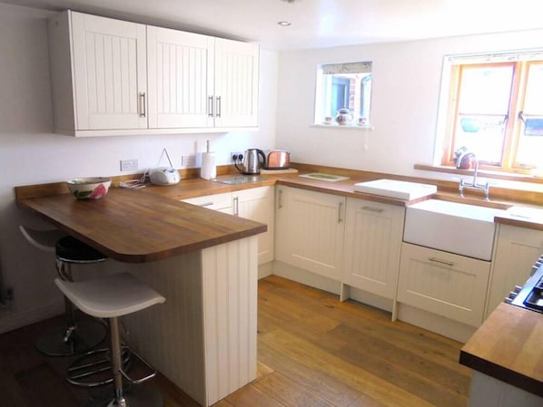 A compact kitchen with wooden countertops, white cabinetry, a built-in island with bar stools, a window with a view, and a sink.