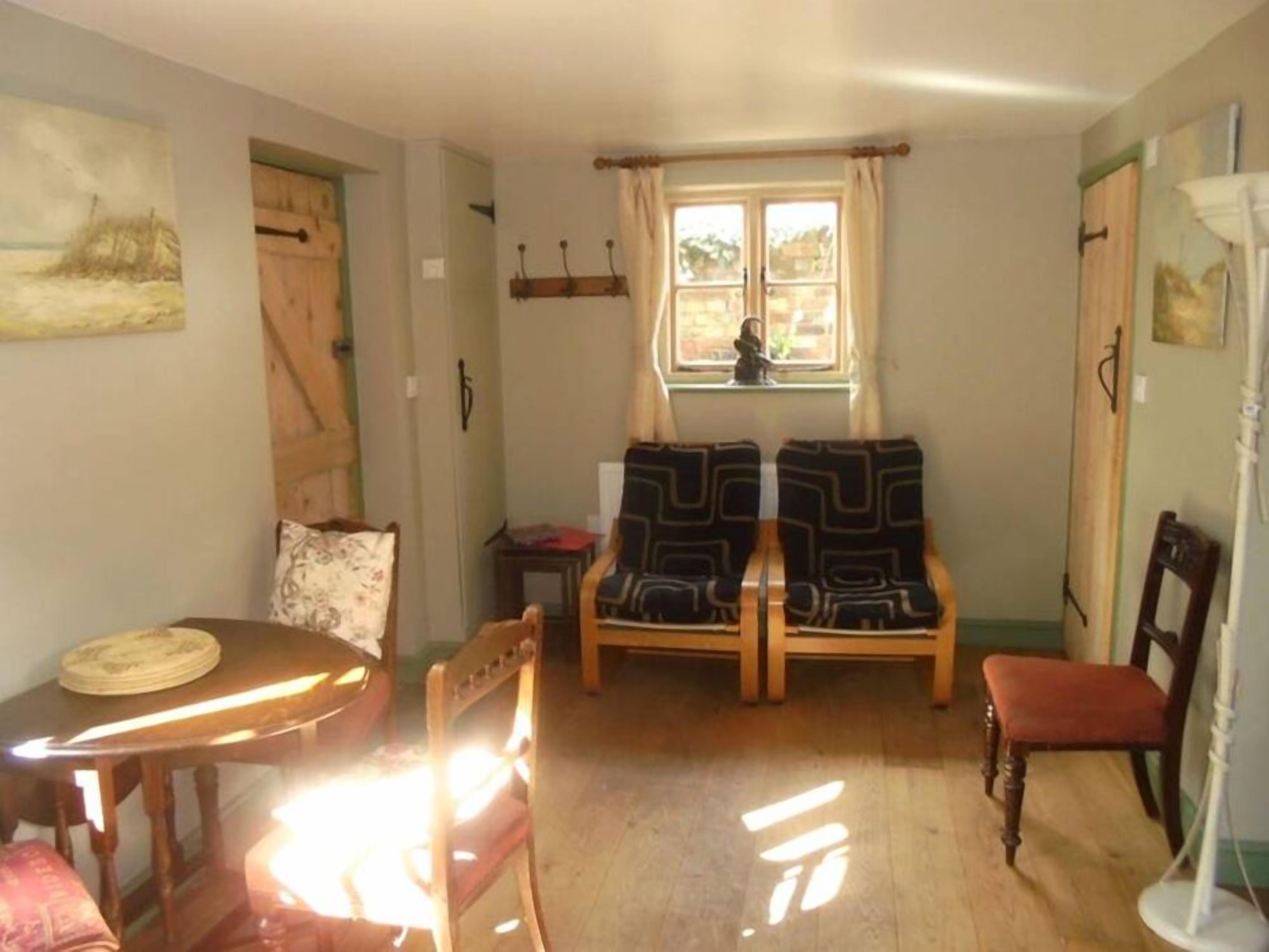 Una habitación acogedora con una mesa de madera, dos sillas estampadas, una mesita con un plato y una ventana con cortinas.