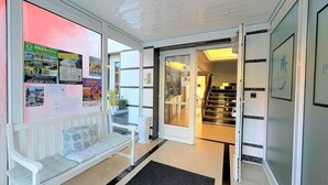 Un vestíbulo de hotel con mostrador de recepción, un banco, una escalera y una pared con varios carteles y anuncios.