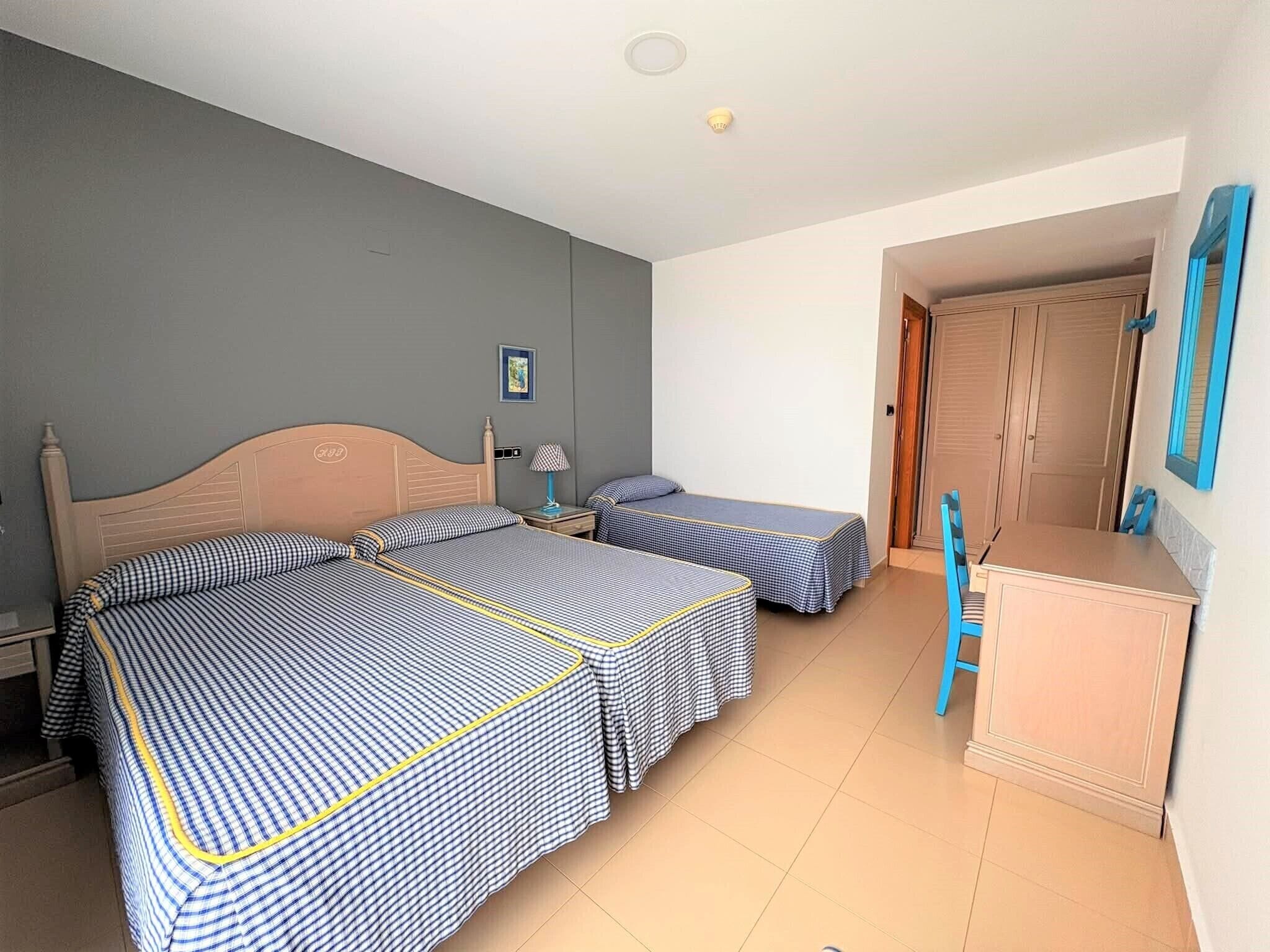A hotel room with two beds, a desk, a chair, a door, and a framed picture on the wall.