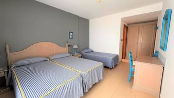 A hotel room with two beds, a desk, a chair, a door, and a framed picture on the wall.