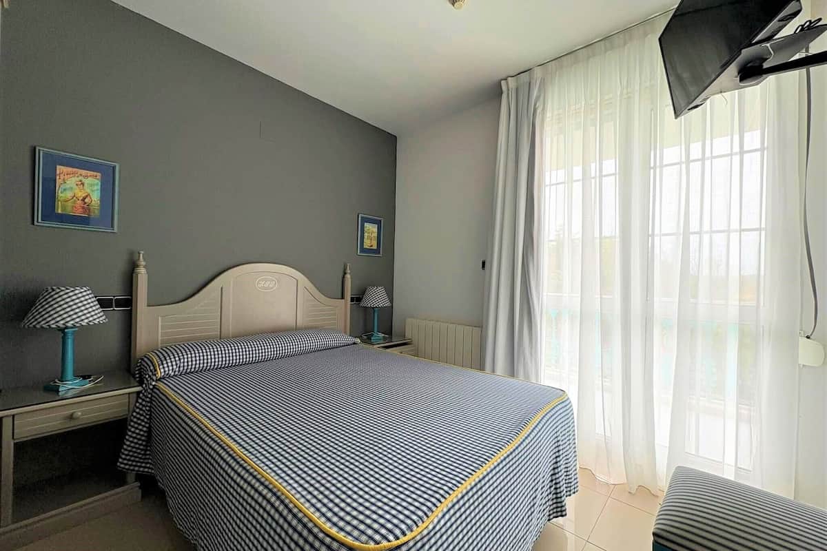 A hotel room with a bed, a desk, a chair, a TV, and a window with curtains.