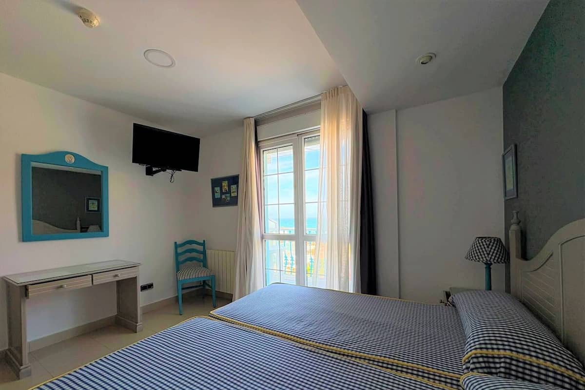A bedroom with a bed, a desk, a chair, a television, and a window with curtains.
