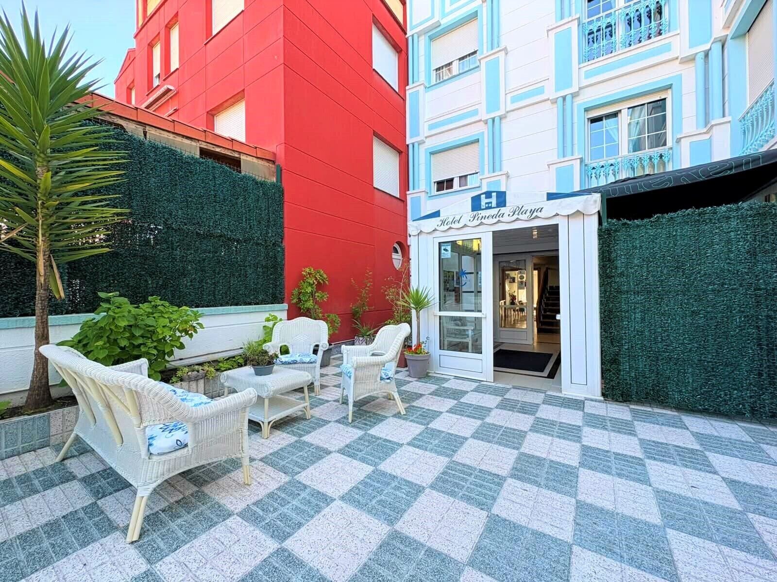 Ein Hotel mit einer Terrasse im Schachbrettmuster, Korbmöbeln und einer Fassade in Rot und Blau.